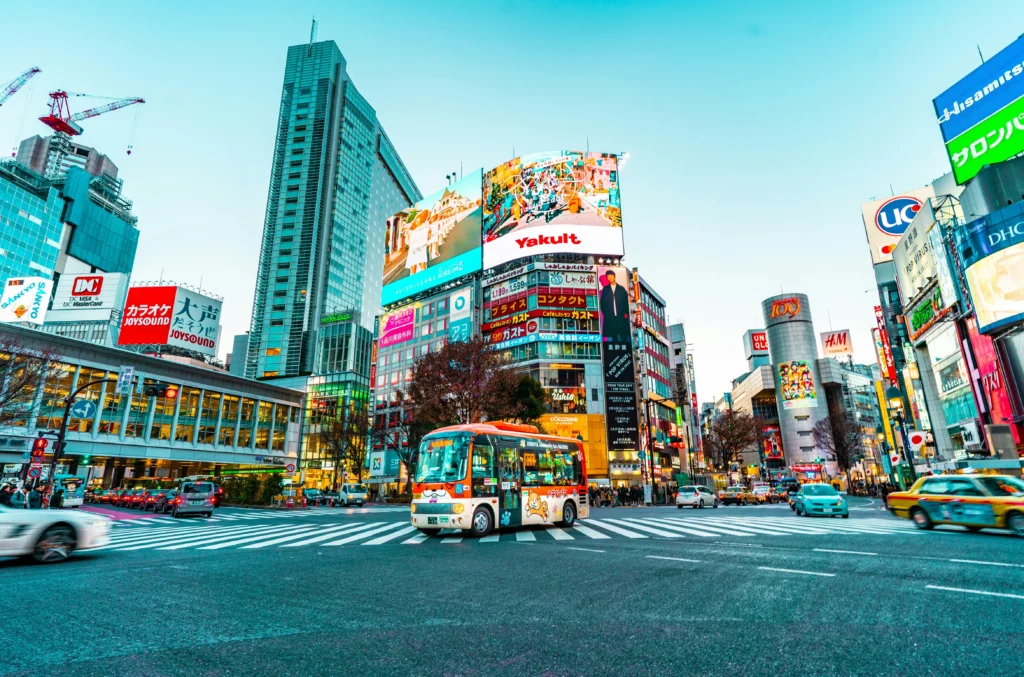 A colorful view of Shibuya Crossing in Tokyo, Japan, with vehicles and pedestrians surrounded by bright billboards and tall buildings.